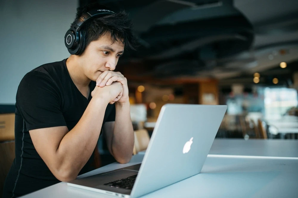 Hispanic audio editor sitting in front of his Apple Macbook