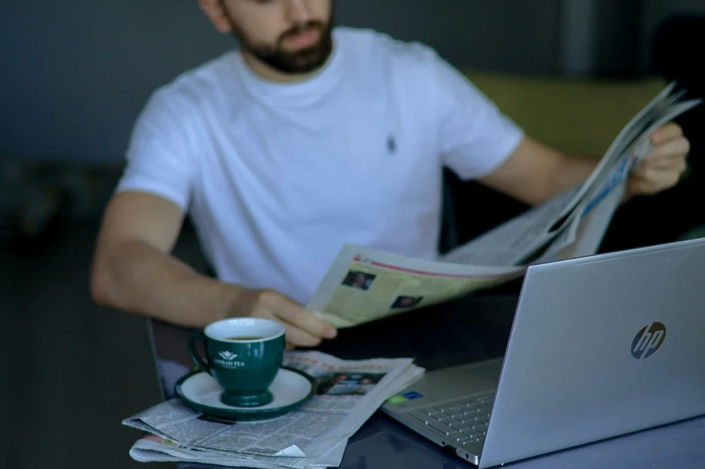 Guy reading news paper at his laptop